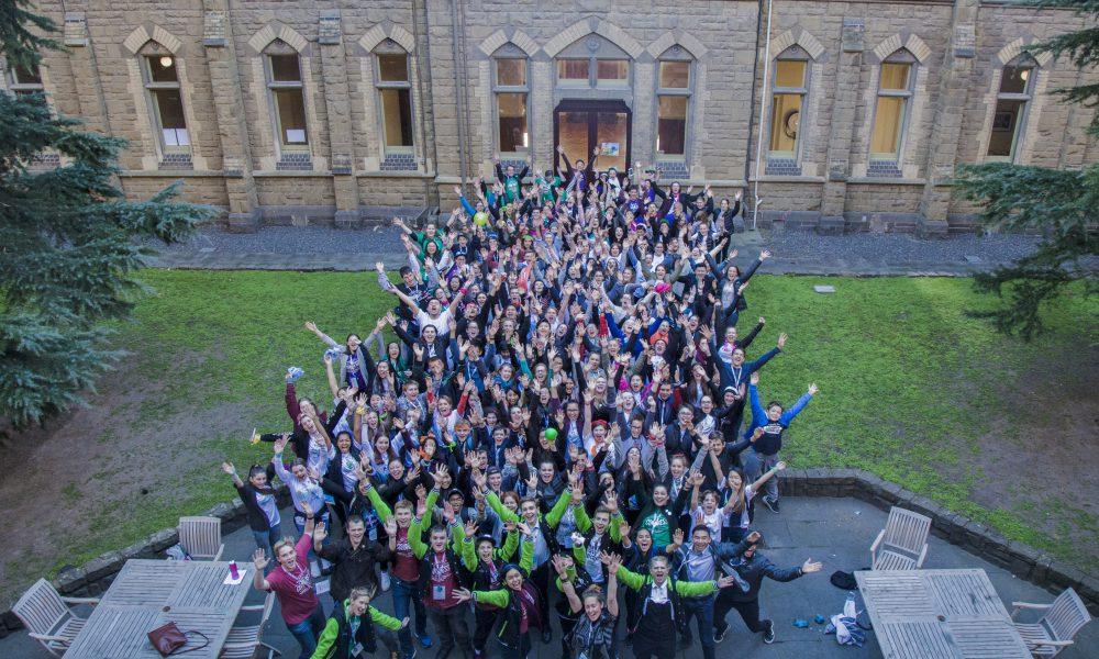 A big group of students stand in a courtyard with their arms raised in celebration.