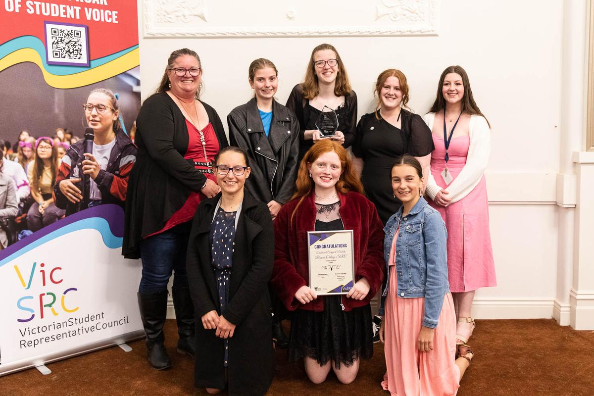 Students and a teacher from Brauer College stand in a group, holding their trophy and certificate.