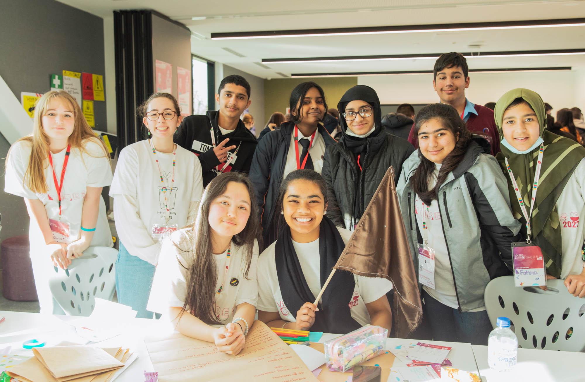 A group of students at VicSRC Congress 2022 stand around a table where they have been working, smiling at the camera.