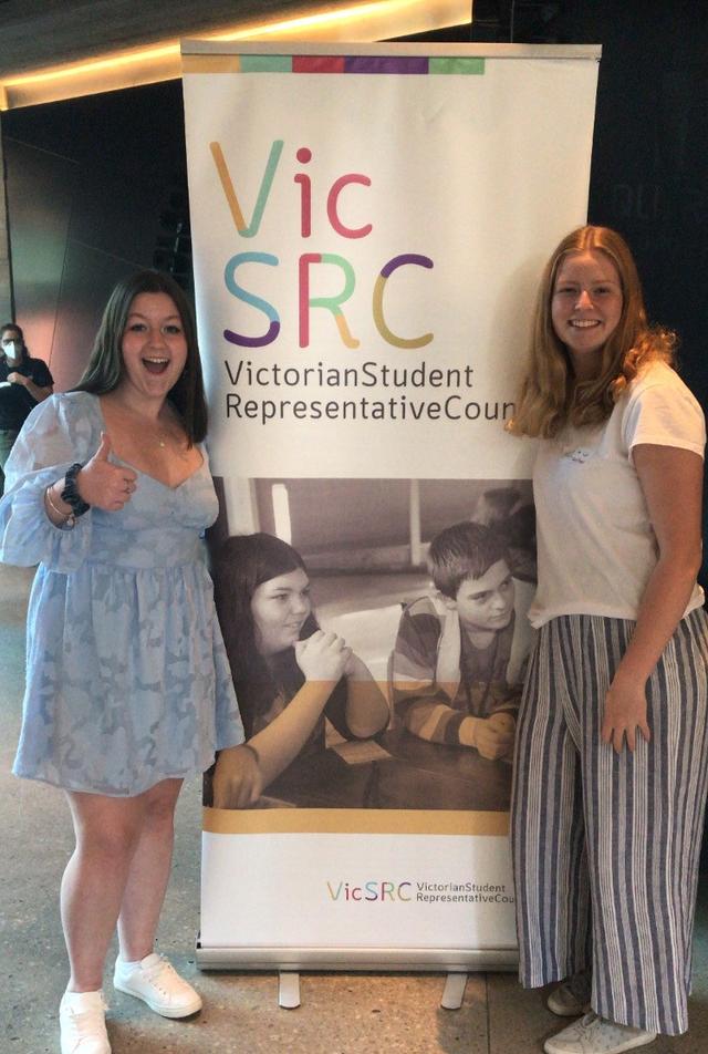 Two ambassadors standing next to a VicSRC banner